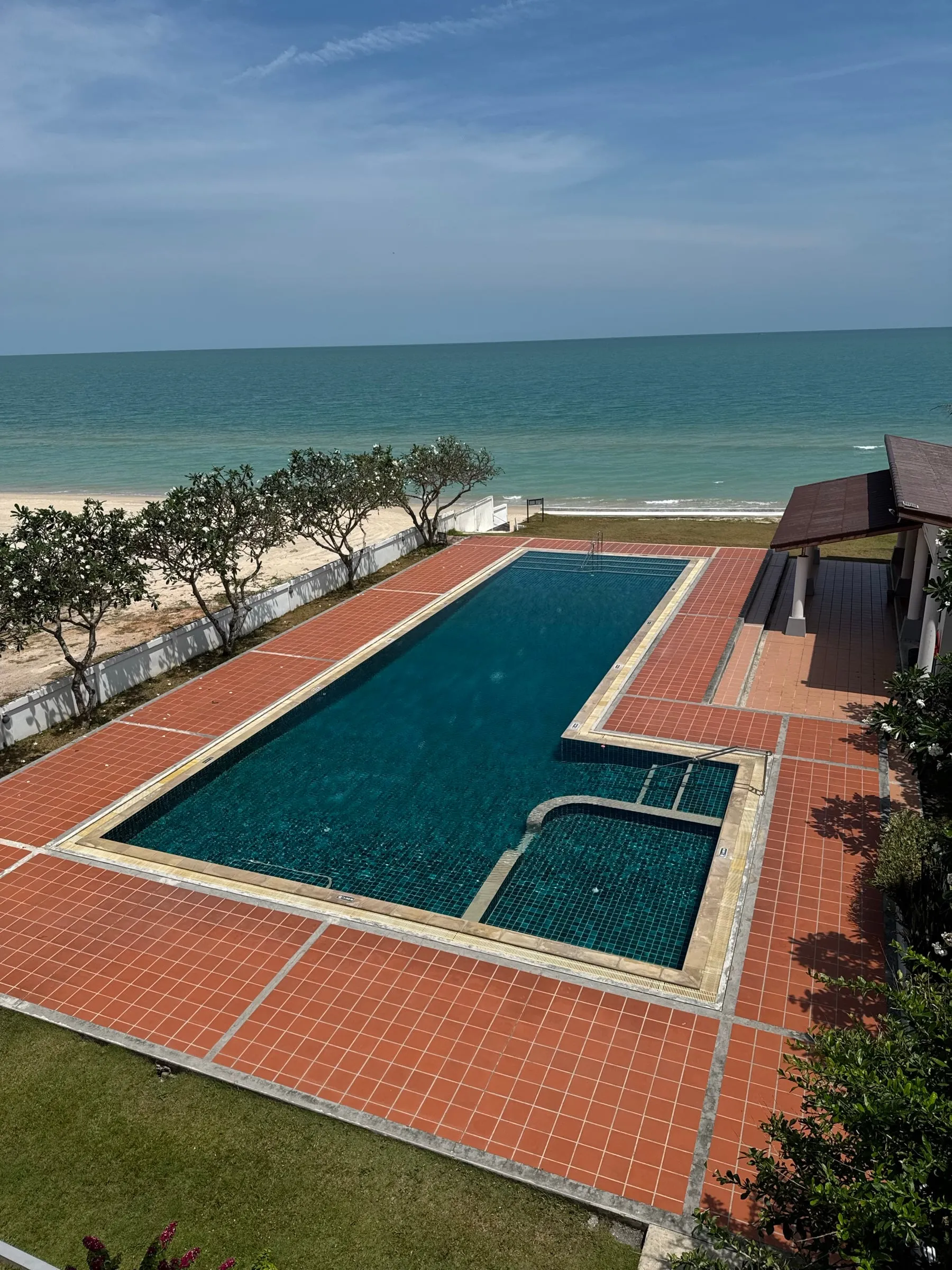 The pool and its terracotta deck seen from an upper floor, frangipani trees and the beach beyond