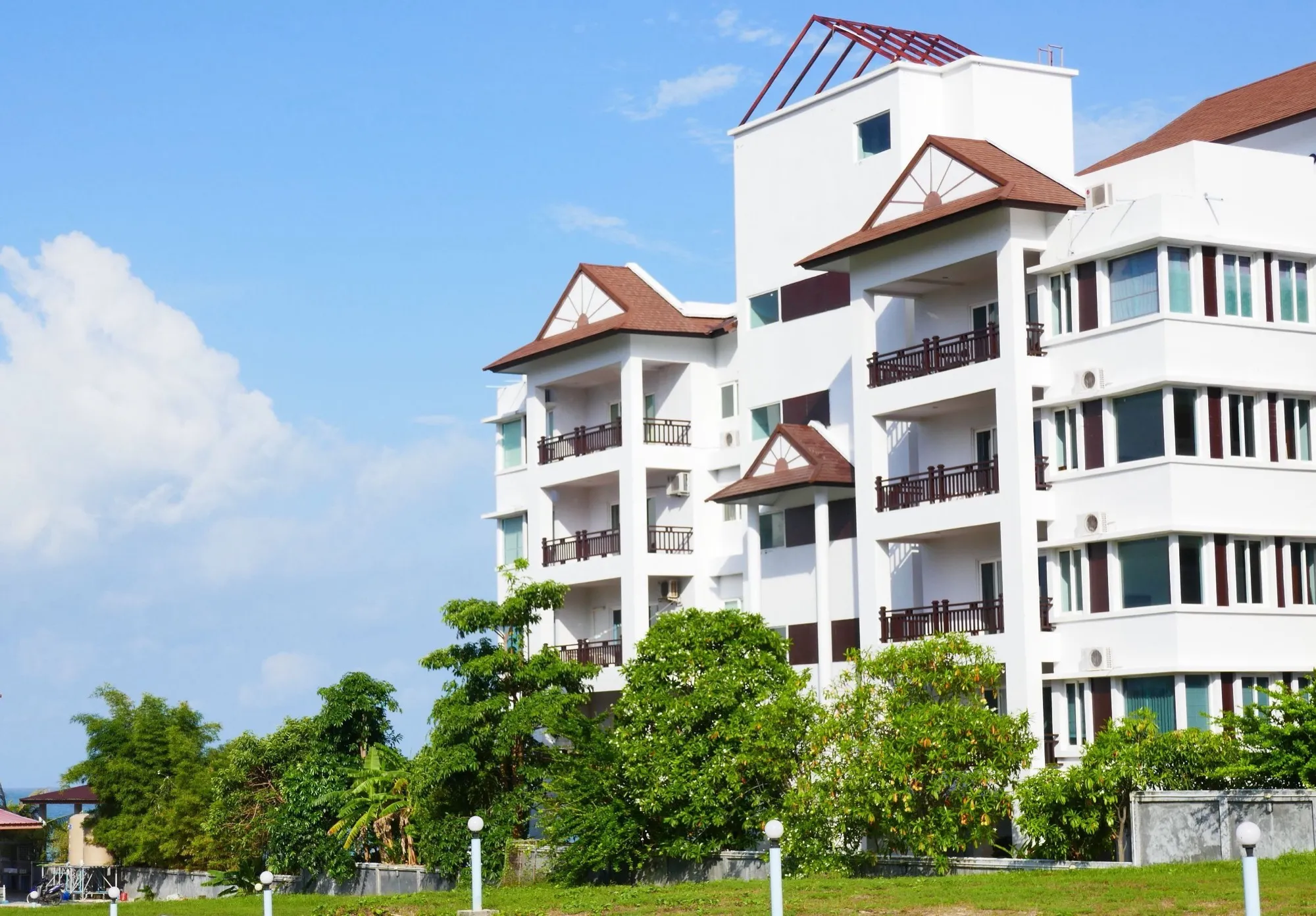 The white building seen from the garden, balconies with dark red railings above the palms and frangipani