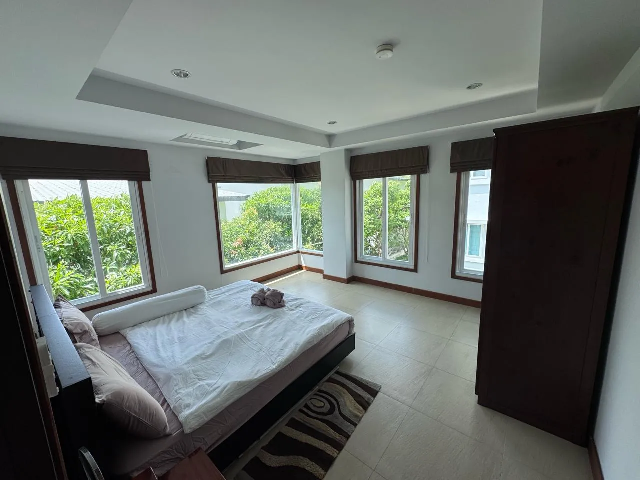 Bedroom with a double bed, a tall wardrobe and corner windows looking into the treetops