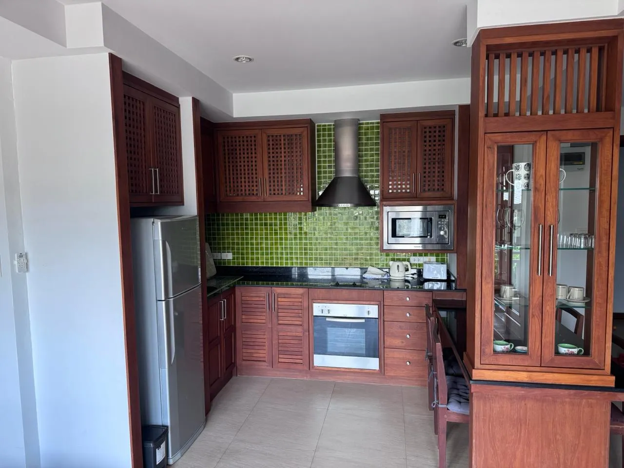 The whole kitchen: fridge, oven, microwave and a glass-fronted dresser beside the dining chairs