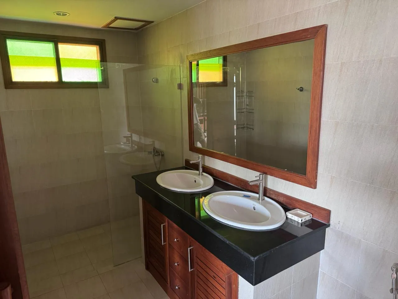 Bathroom with two basins on a dark stone counter and a glass-walled shower